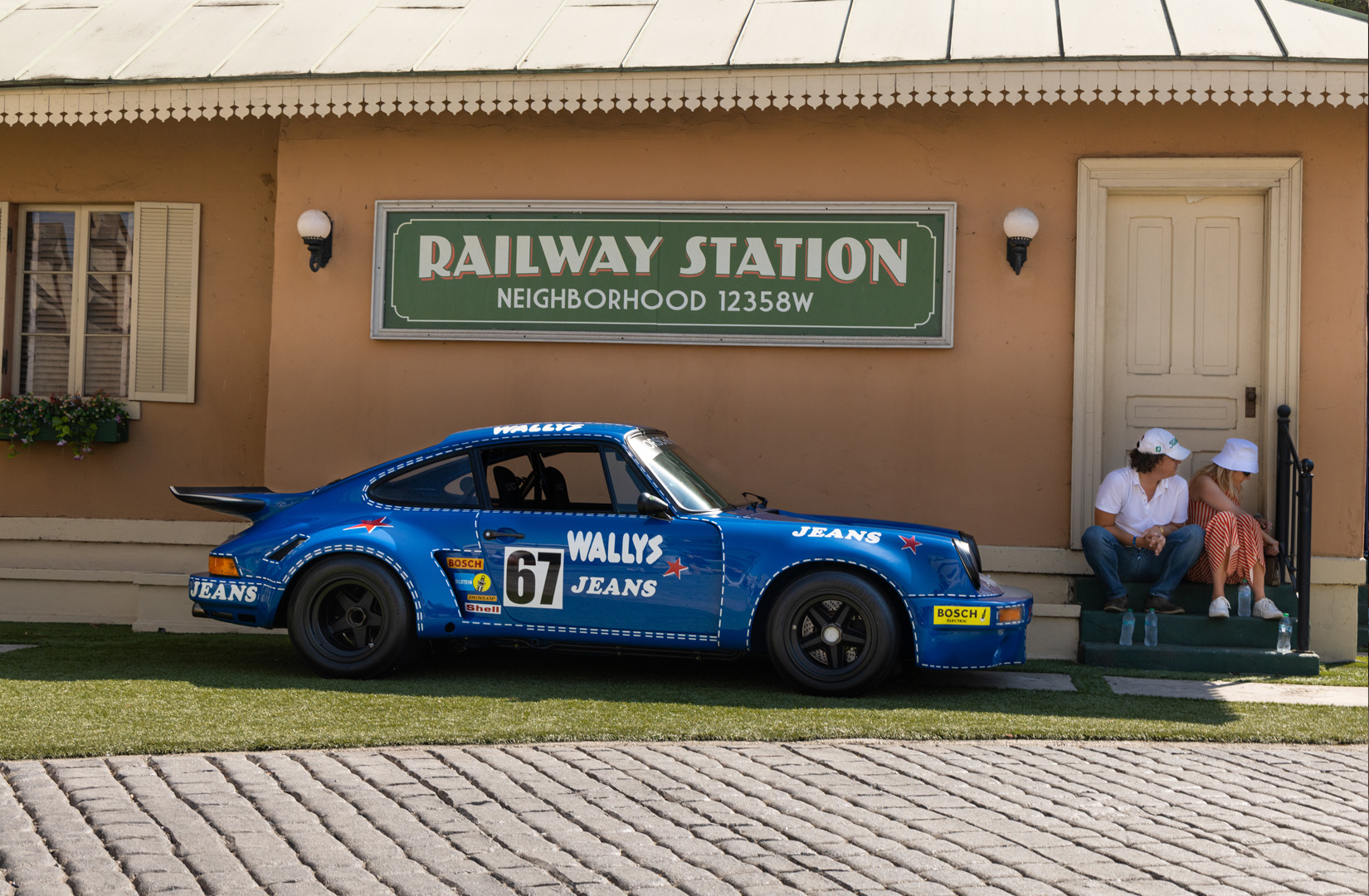 Couple sitting on stoop next to parked blue Porsche
